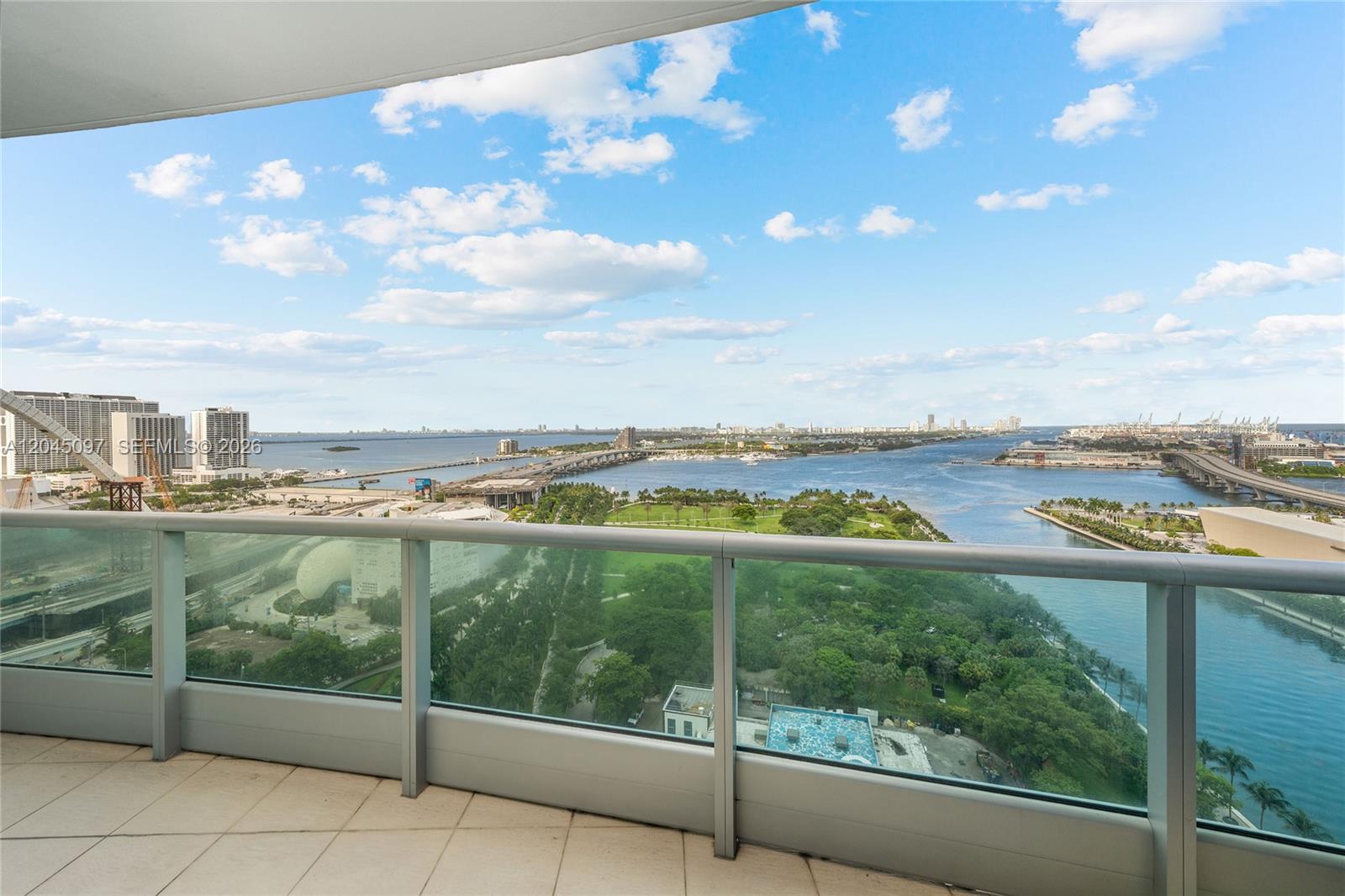 A balcony with a glass railing overlooks a park, a bridge, and a body of water — 900 Biscayne Blvd # 2506, Miami FL 33132, MIAMI, FL