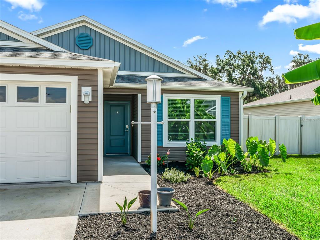 A single-story house exterior features brown siding, a teal front door, and a white garage — 4438 CAMEO CIRCLE, THE VILLAGES, FL