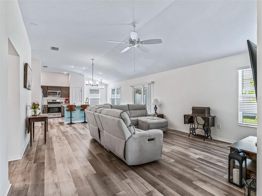An open-concept living room and kitchen featuring light wood-look flooring and a grey sectional sofa — 4438 CAMEO CIRCLE, THE VILLAGES, FL