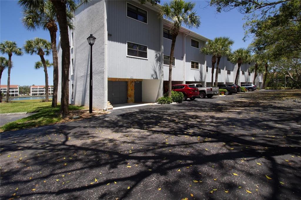 A multi-story gray building with covered parking and palm trees sits beside an asphalt lot — 12140 CAPRI CIRCLE S UNIT 709, TREASURE ISLAND, FL