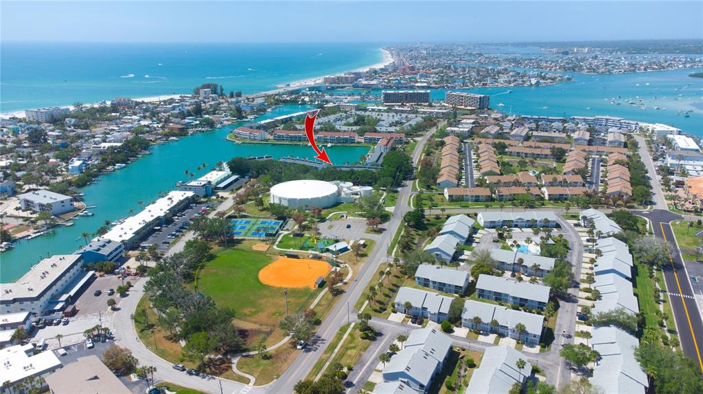 Aerial view of a coastal residential complex featuring a large circular building and sports fields — 12140 CAPRI CIRCLE S UNIT 709, TREASURE ISLAND, FL