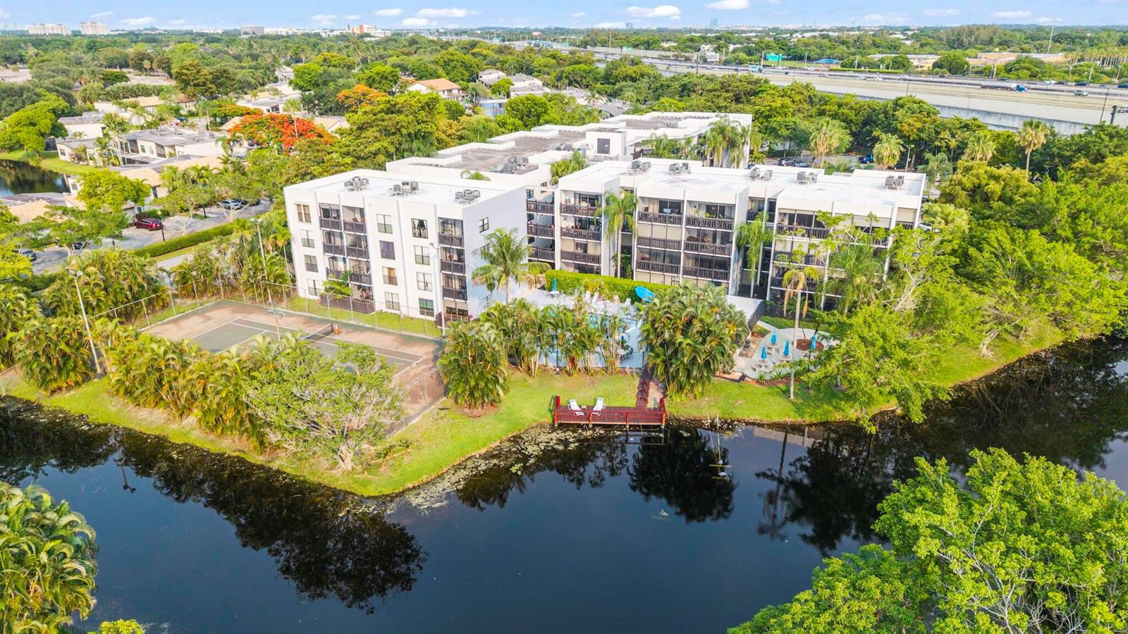 An aerial view of a multi-story apartment complex with a tennis court, pool, and lake — 1021 Mockingbird Lane # 211, Plantation FL 33324, PLANTATION, FL