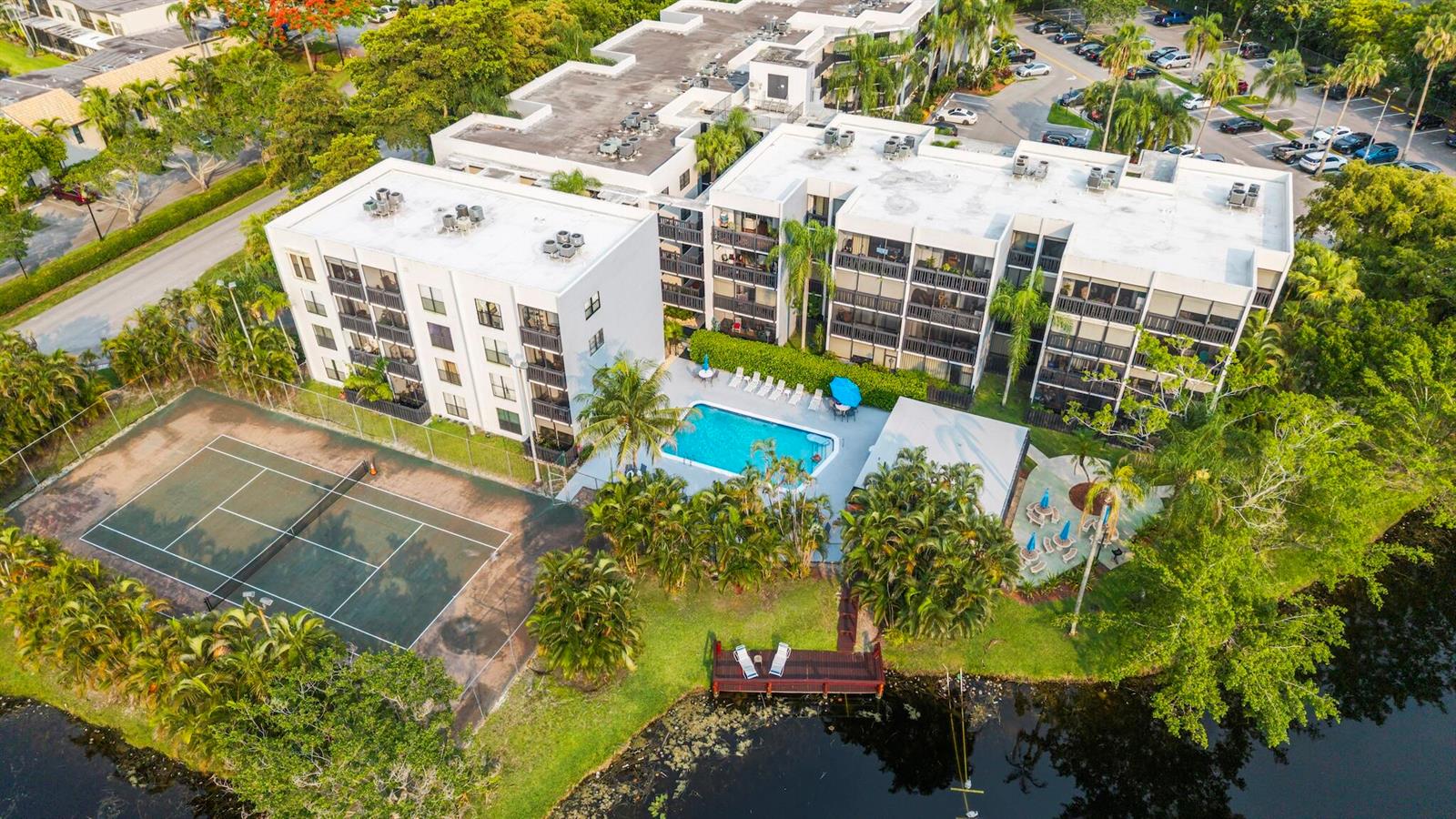 An aerial view of an apartment complex featuring a swimming pool, tennis court, and lake — 1021 Mockingbird Lane # 211, Plantation FL 33324, PLANTATION, FL