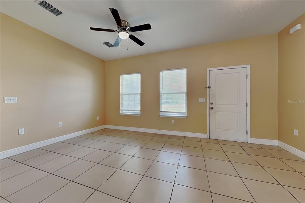 An empty room features tan walls, tiled flooring, a ceiling fan, two windows, and a door — 5017 SW 165TH STREET ROAD, OCALA, FL