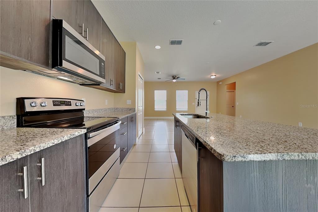 A kitchen features dark wood cabinets, granite countertops, stainless steel appliances, and tile flooring — 5017 SW 165TH STREET ROAD, OCALA, FL