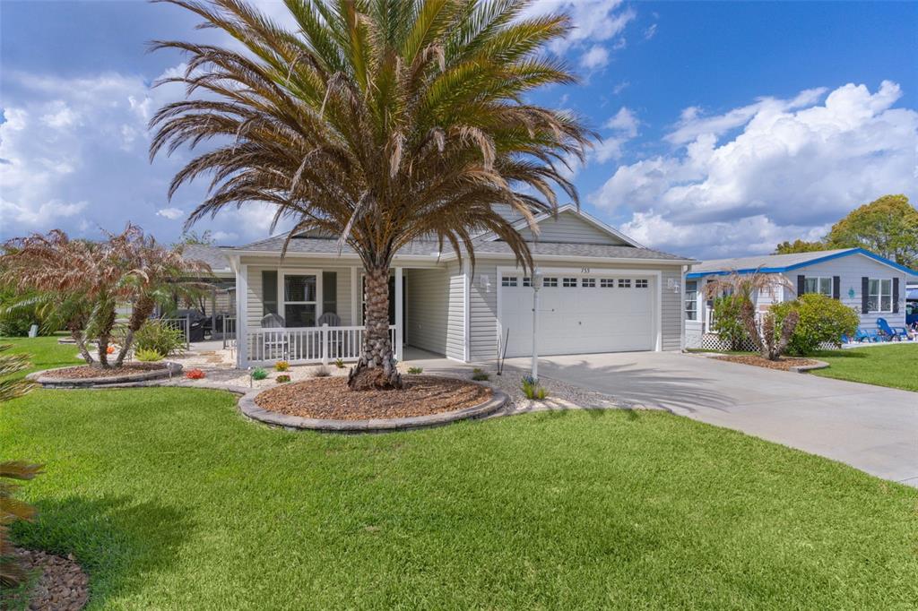 A single-story house with light siding, a white garage door, and a prominent palm tree — 733 JASON DRIVE, THE VILLAGES, FL