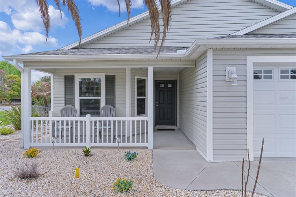 A light gray house exterior features a covered front porch with two chairs and gravel — 733 JASON DRIVE, THE VILLAGES, FL