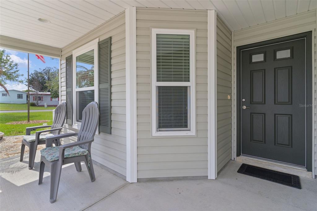 A covered front porch features light gray siding, two plastic chairs, and a dark front door — 733 JASON DRIVE, THE VILLAGES, FL