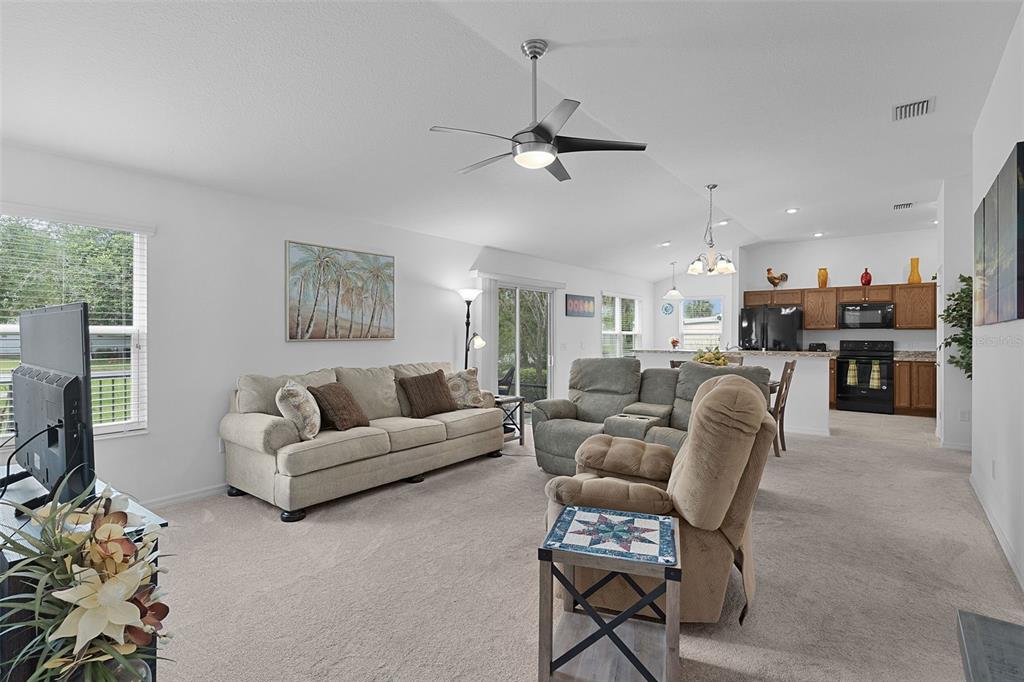A living room with beige carpet, a sofa, a recliner, and an open-concept kitchen — 733 JASON DRIVE, THE VILLAGES, FL
