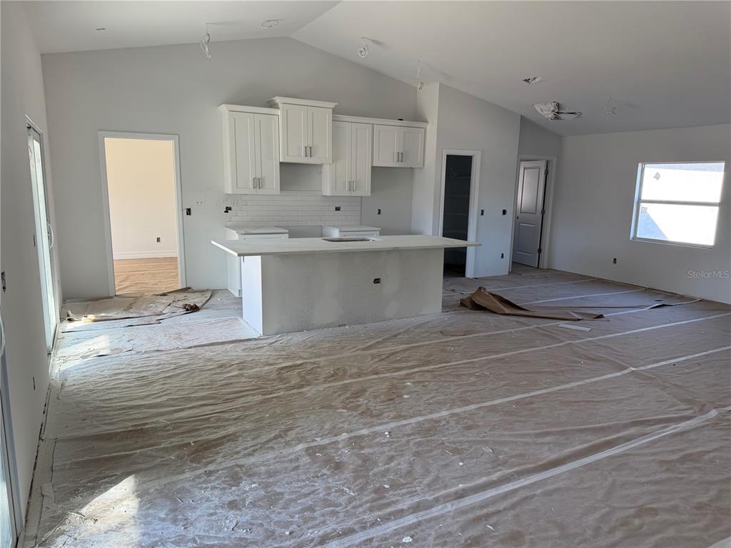 An unfinished kitchen features white cabinets, a central island, and protective paper covering the floor — 15061 MCGRAW AVENUE, PORT CHARLOTTE, FL
