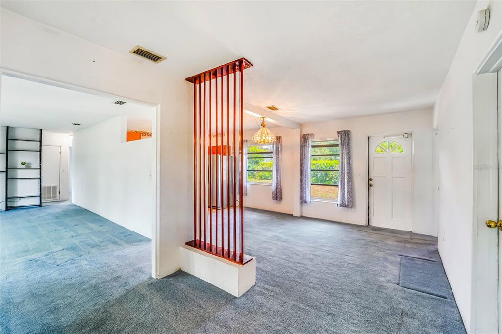 A living room with blue carpet, a red vertical slat room divider, and a front door — 1326 ST THOMAS DRIVE, CLEARWATER, FL