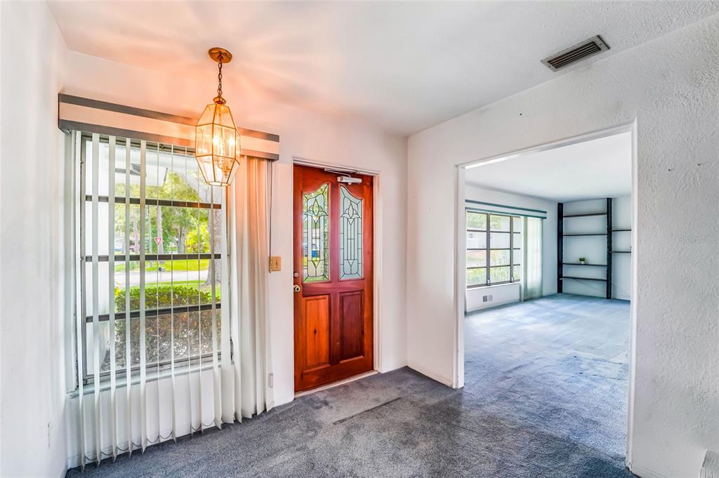 An entryway with gray carpet, a wooden front door, and a hanging pendant light fixture — 1326 ST THOMAS DRIVE, CLEARWATER, FL