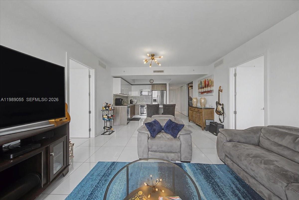 A living room with white tile floors flows into an open-concept kitchen with stainless appliances — 5252 NW 85th Ave # 1410, Doral FL 33166, DORAL, FL