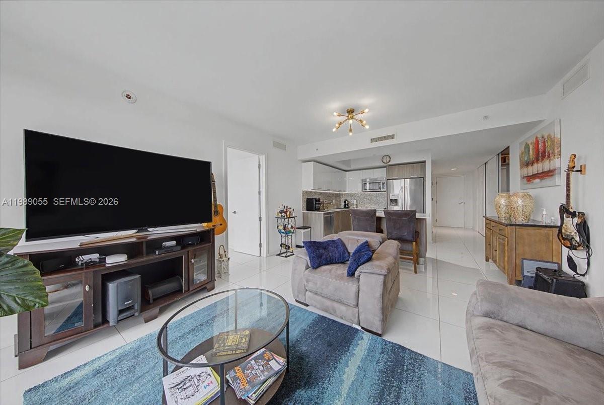 This living room features a large television, a blue area rug, and an open kitchen — 5252 NW 85th Ave # 1410, Doral FL 33166, DORAL, FL
