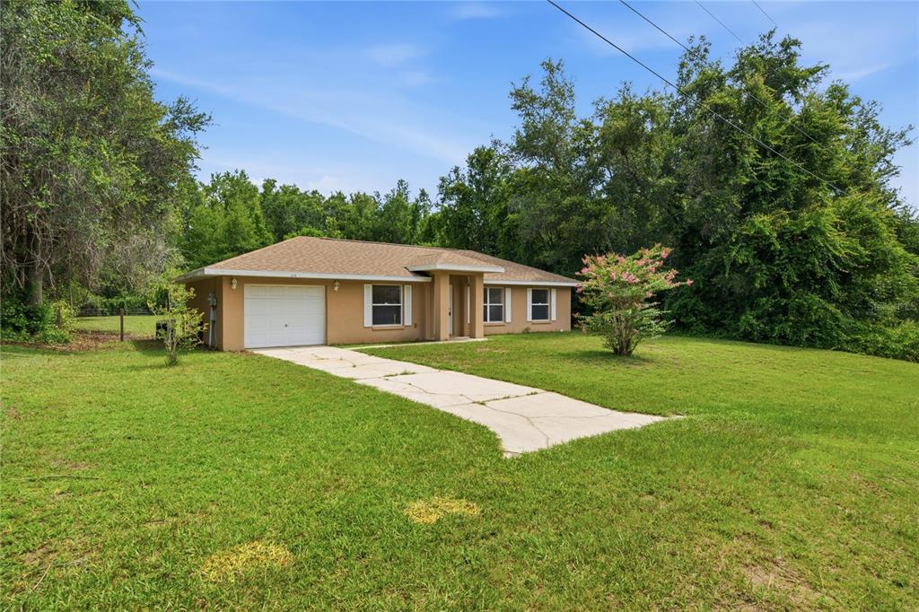 A single-story tan house with a one-car garage and a concrete driveway sits on grass — 2210 BLUEGRASS ST, INVERNESS, FL