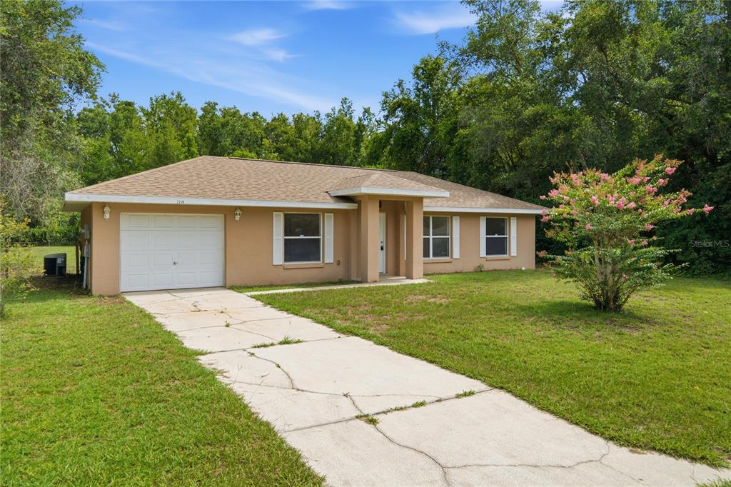 A single-story tan house with a white garage door and a concrete driveway — 2210 BLUEGRASS ST, INVERNESS, FL