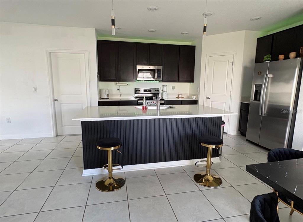 A kitchen features dark cabinets, a white-topped island with black paneling, and two barstools — 626 BELL PRAIRIE CIRCLE, LAKE WALES, FL