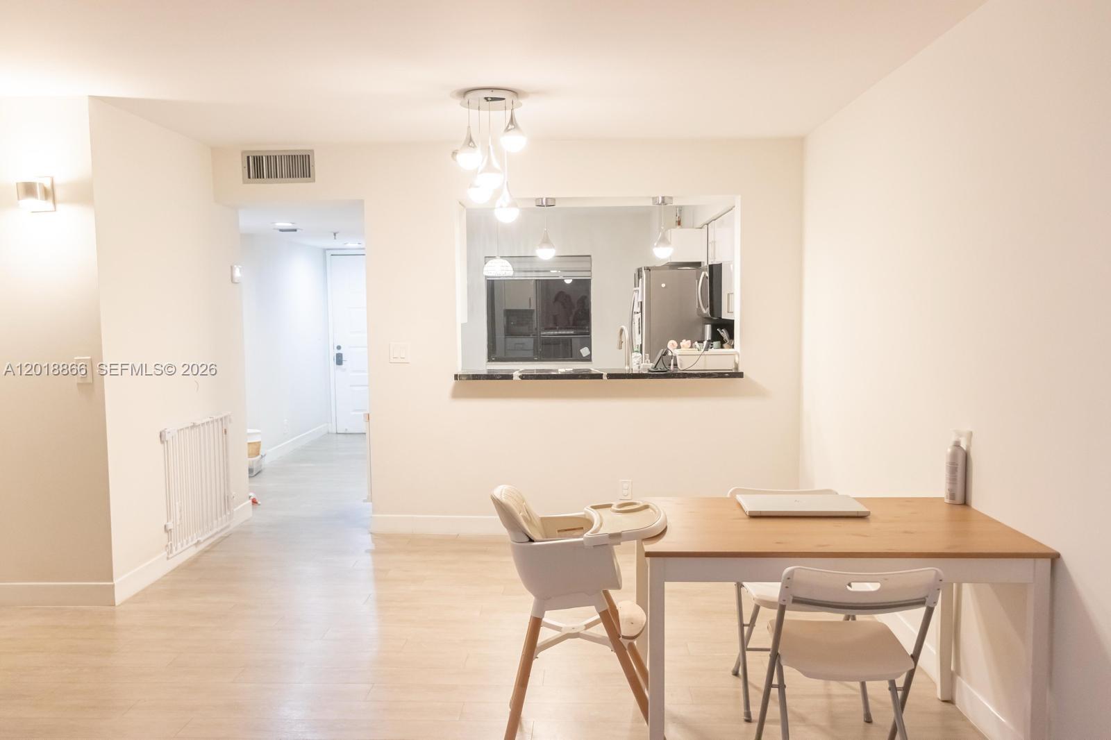 A dining area features a light wood table, a high chair, and a kitchen pass-through window — 2200 S Cypress Bend Dr # 204, Pompano Beach FL 33069, POMPANO BEACH, FL