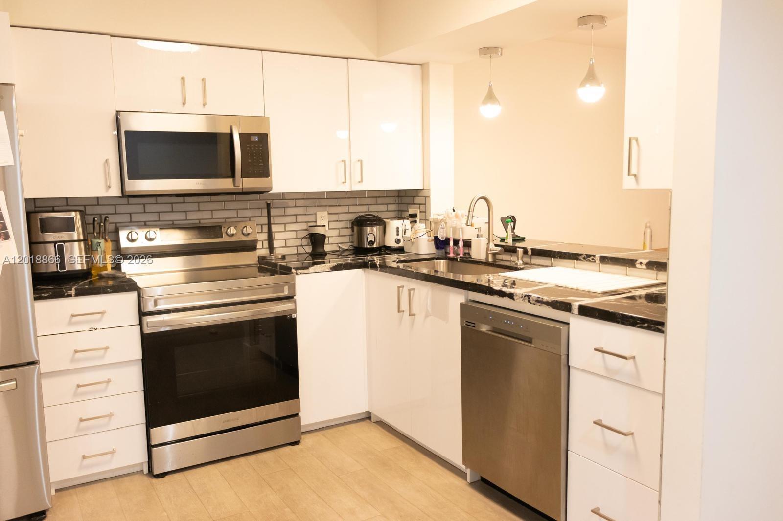 A kitchen features white cabinets, stainless steel appliances, and a black and white countertop — 2200 S Cypress Bend Dr # 204, Pompano Beach FL 33069, POMPANO BEACH, FL