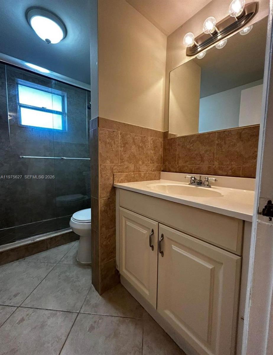 A bathroom features a vanity with a white countertop, a mirror, and a glass-enclosed shower — 1100 NE 1st Ct # 312, Hallandale Beach FL 33009, HALLANDALE BEACH, FL