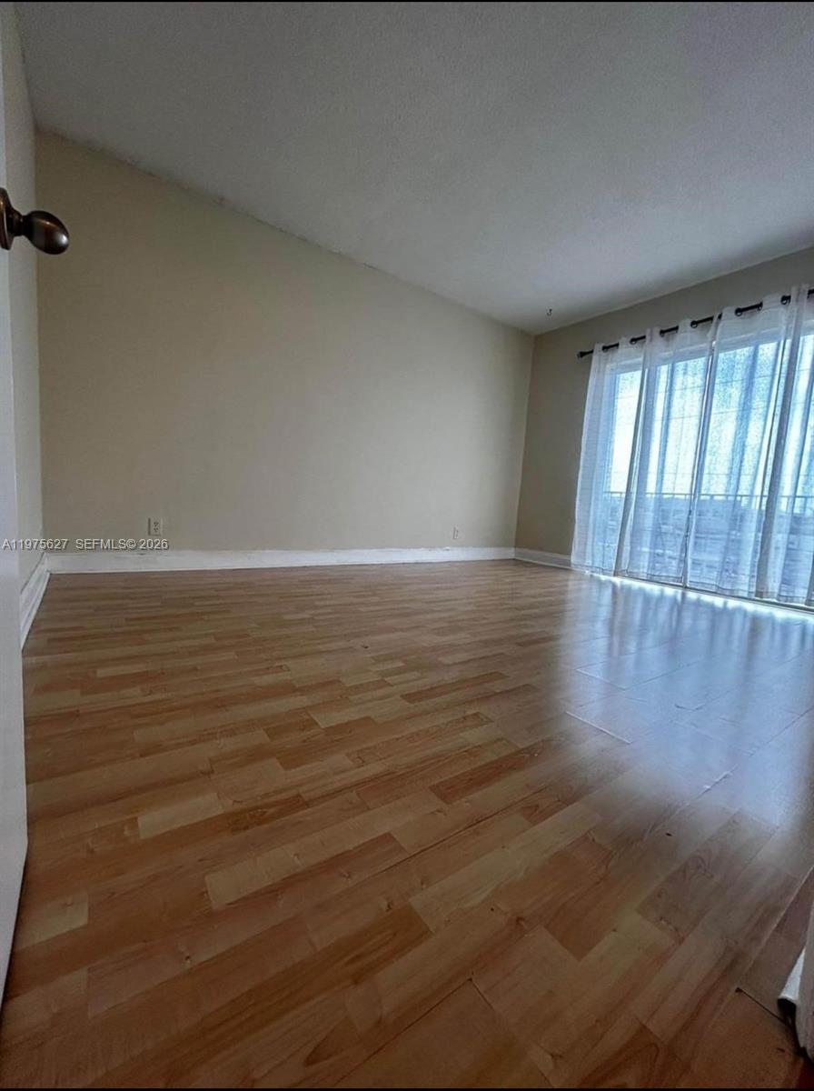 An empty room features light-colored wood-look flooring, beige walls, and a large sliding glass door — 1100 NE 1st Ct # 312, Hallandale Beach FL 33009, HALLANDALE BEACH, FL
