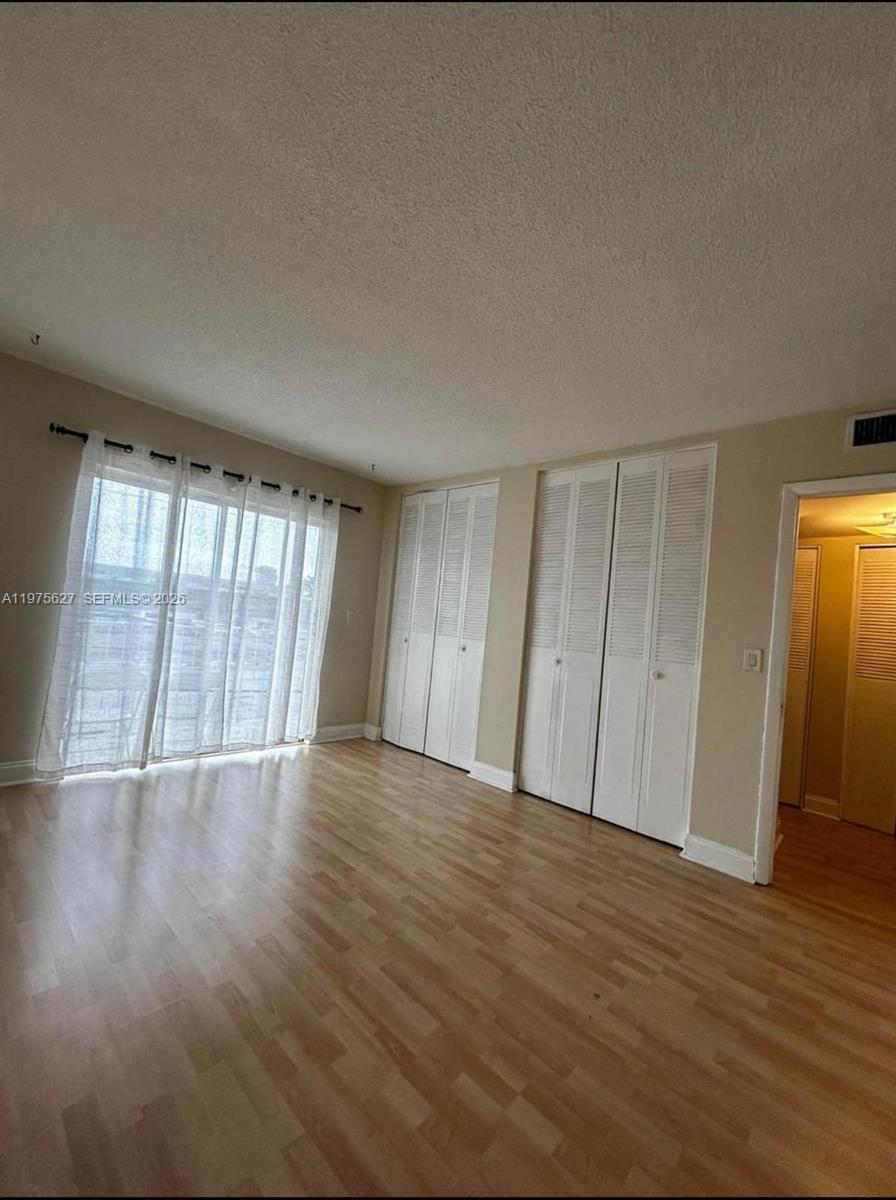 An empty room features light wood-look flooring, white louvered closet doors, and a sliding glass door — 1100 NE 1st Ct # 312, Hallandale Beach FL 33009, HALLANDALE BEACH, FL