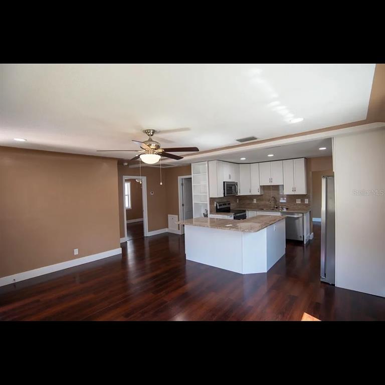 A kitchen with white cabinets and a granite island opens into a living area — 1329 34TH AVENUE N, ST PETERSBURG, FL