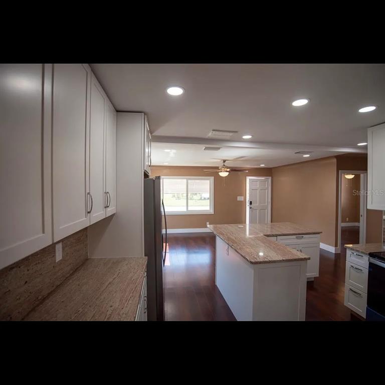A kitchen with white cabinets, granite countertops, and an island overlooking a living area — 1329 34TH AVENUE N, ST PETERSBURG, FL