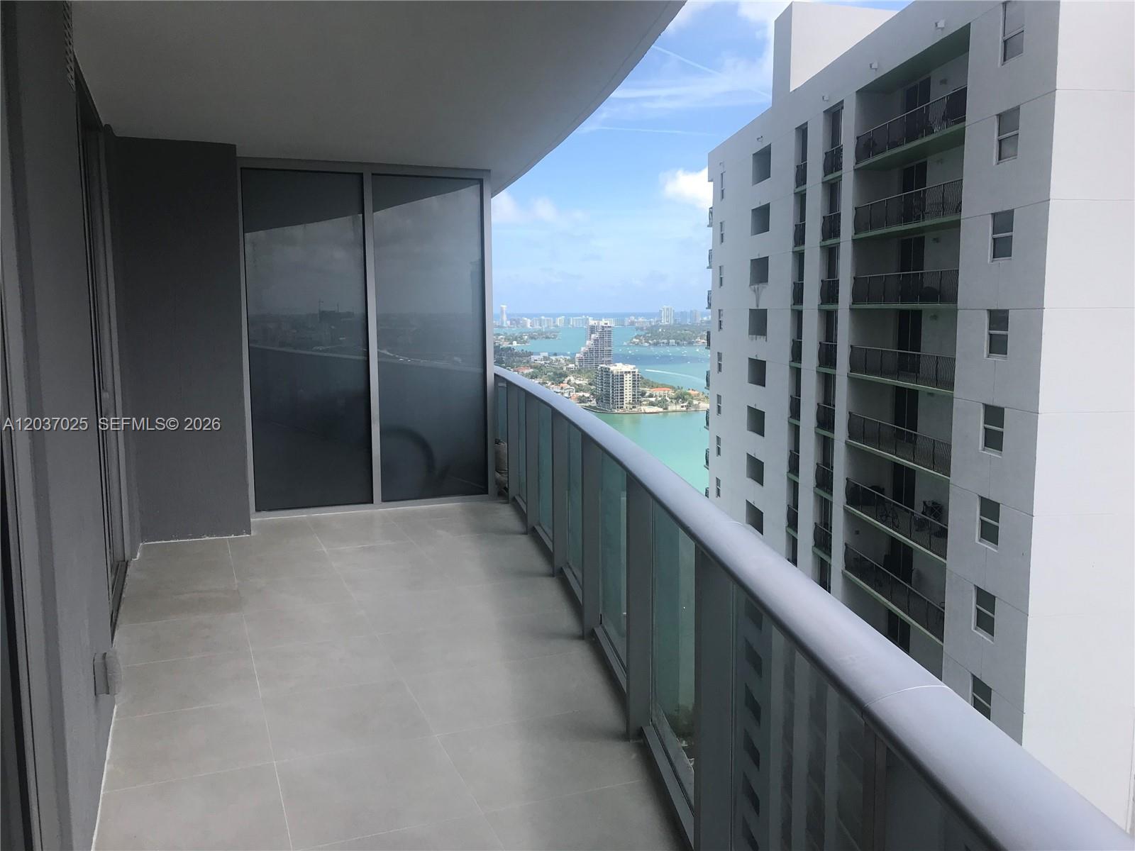 A balcony with gray tile flooring overlooks a bay and a neighboring high-rise building — 488 NE 18th St # 3102, Miami FL 33132, MIAMI, FL