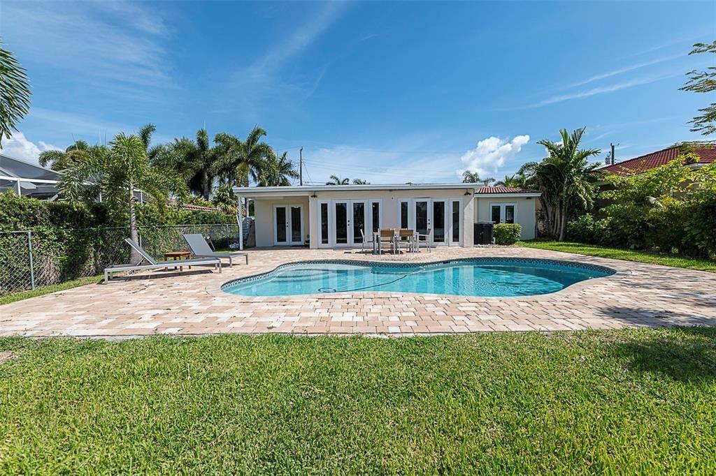 A backyard features a swimming pool, a paved patio, and a house with glass doors — 1162 Hayes Street, Hollywood FL 33019, HOLLYWOOD, FL