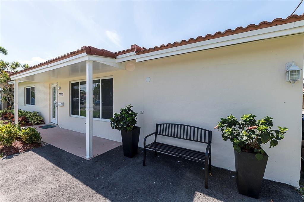 A beige house exterior features a covered porch, a black metal bench, and potted plants — 1162 Hayes Street, Hollywood FL 33019, HOLLYWOOD, FL