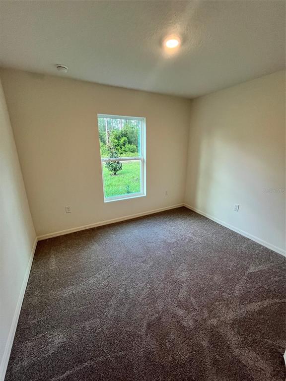 A bedroom with beige walls, brown carpet, a single window, and a ceiling light fixture — 10540 YEAGER AVENUE, HASTINGS, FL