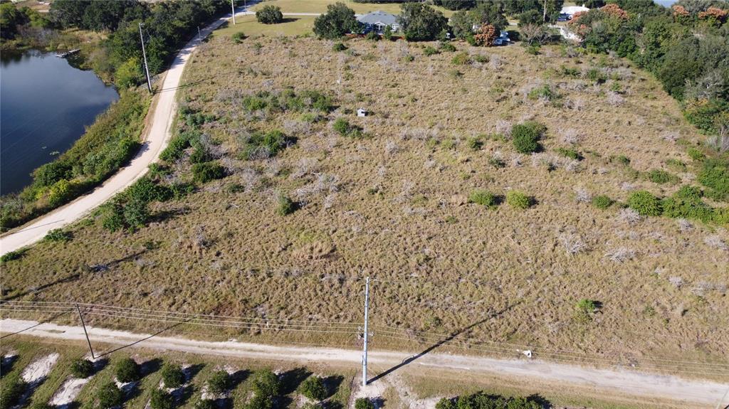 An aerial view shows a large, undeveloped grassy lot bordering a lake and a dirt road — 600 GROVE AVENUE, LAKE WALES, FL