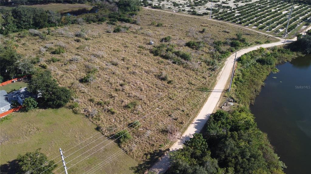 An aerial view shows a vacant, grassy lot bordered by a dirt road and water — 600 GROVE AVENUE, LAKE WALES, FL