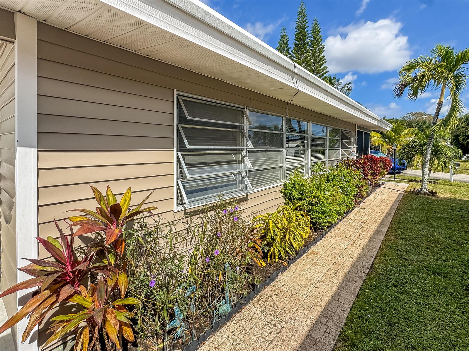 The exterior of a beige house features horizontal siding, jalousie windows, and a landscaped garden — 14553 Elmhurst Drive, Delray Beach FL 33445, DELRAY BEACH, FL
