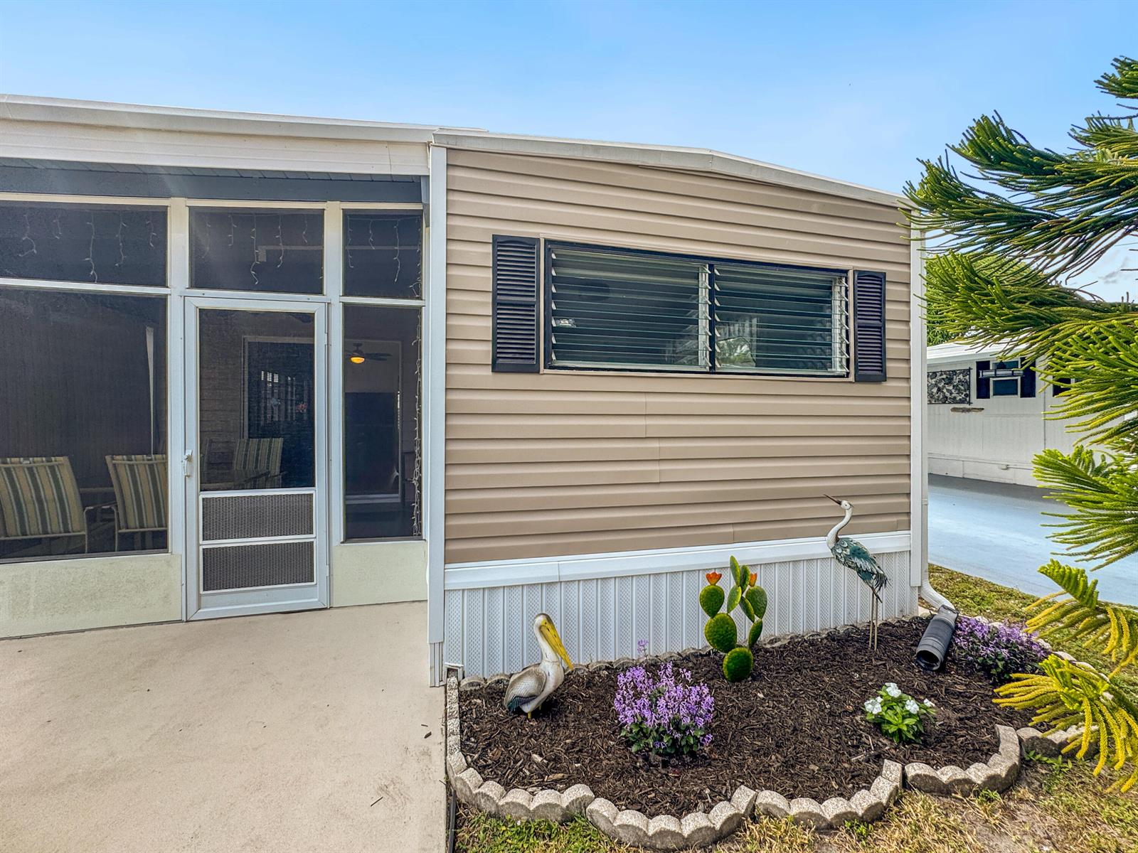 A tan mobile home features a screened-in porch, louvered windows, and a landscaped garden bed — 14553 Elmhurst Drive, Delray Beach FL 33445, DELRAY BEACH, FL