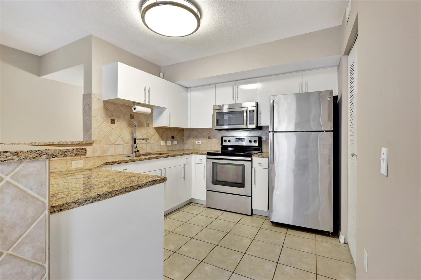 A kitchen with white cabinets, granite countertops, stainless steel appliances, and beige tile flooring — 310 Villa Circle # 310, Boynton Beach FL 33435, BOYNTON BEACH, FL