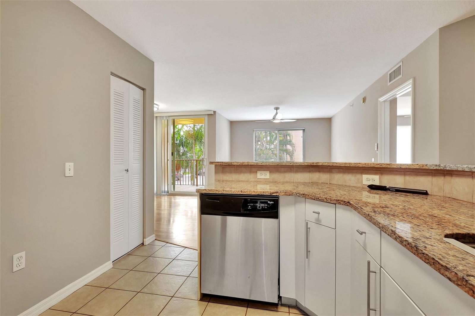 A kitchen with stainless steel dishwasher, granite countertops, and tile flooring overlooks a living area — 310 Villa Circle # 310, Boynton Beach FL 33435, BOYNTON BEACH, FL