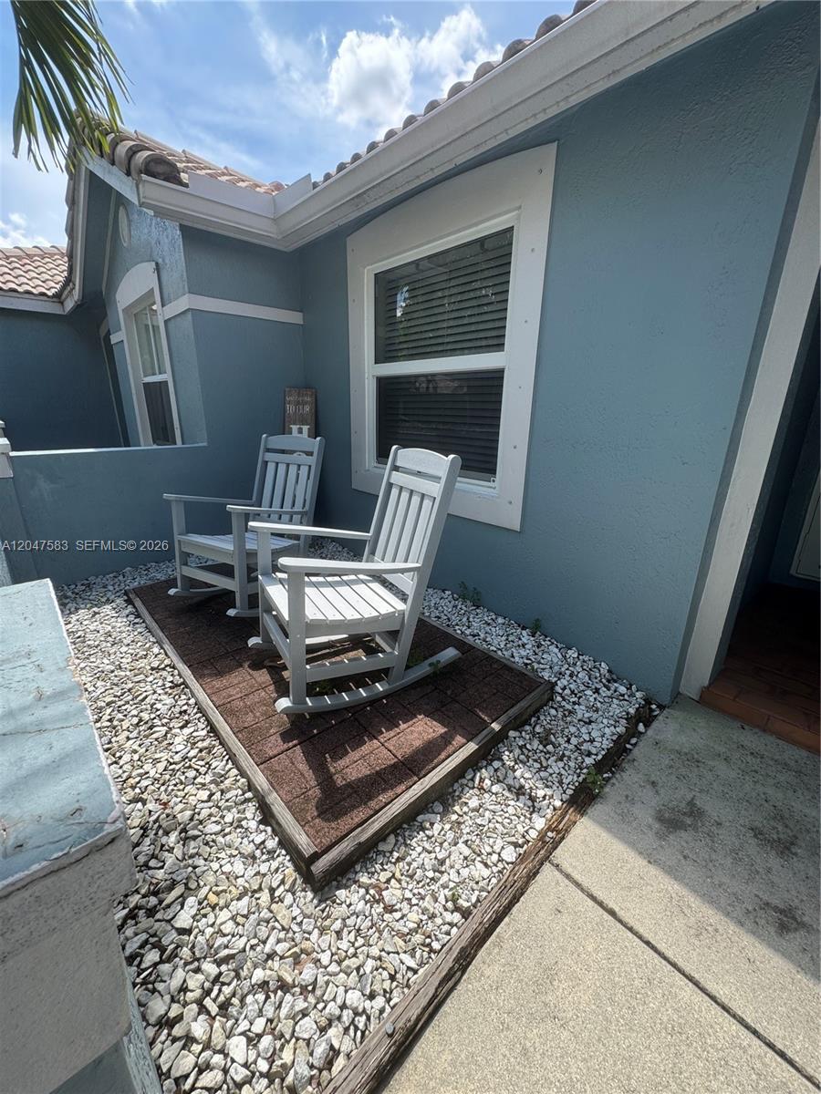 Two white rocking chairs sit on a small patio area with gravel and pavers — 4152 Pine Ridge Ln # 0, Weston FL 33331, WESTON, FL