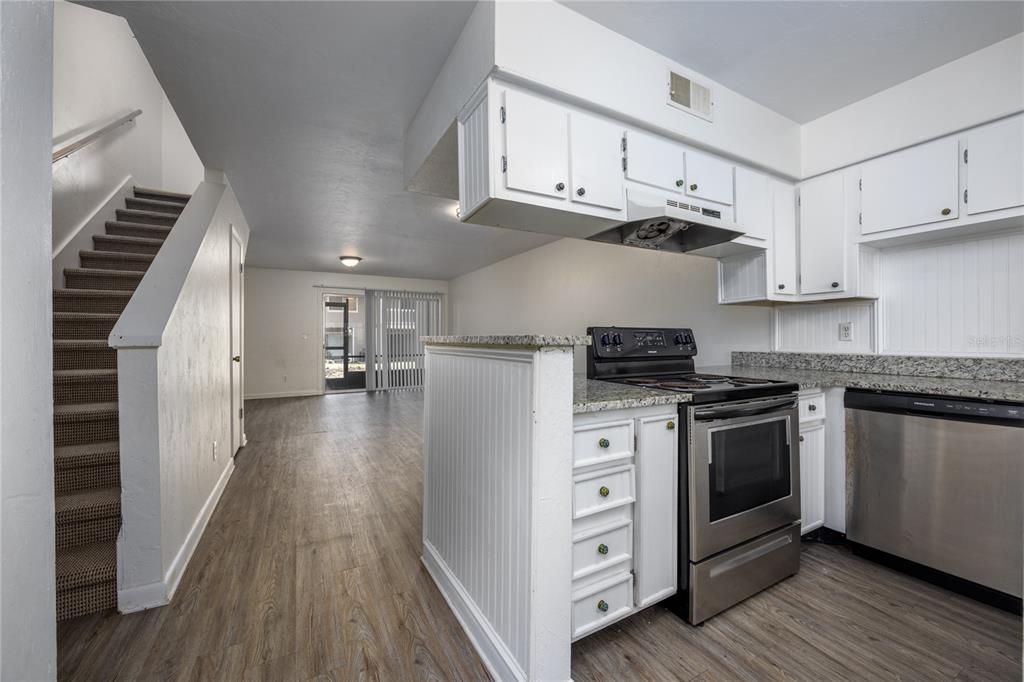 A kitchen with white cabinets and stainless steel appliances overlooks a living area with stairs — 4411 SW 34TH STREET UNIT 908, GAINESVILLE, FL