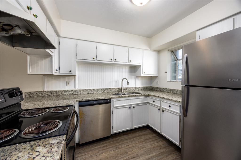 A kitchen features white cabinets, granite countertops, stainless steel appliances, and wood-look flooring — 4411 SW 34TH STREET UNIT 908, GAINESVILLE, FL
