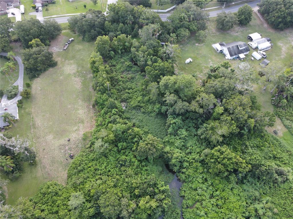 An aerial view shows a large, wooded lot with a stream and adjacent residential properties — 1401 N FULLERS CROSS ROAD, WINTER GARDEN, FL