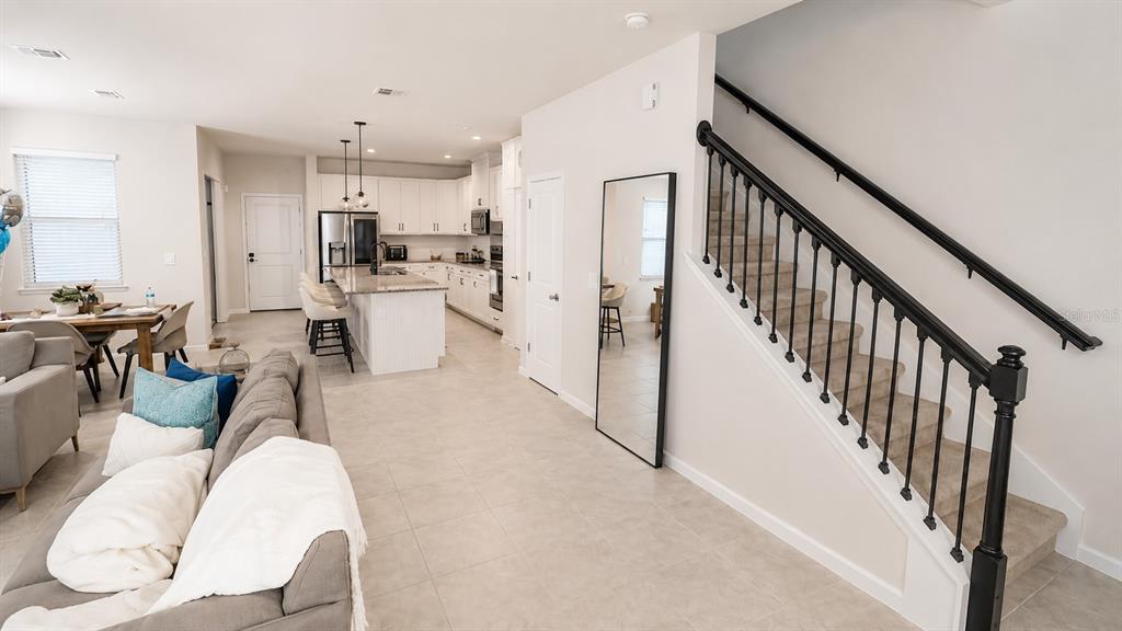 An open-concept living room and kitchen featuring a staircase with black railings and tile flooring — 3974 GREAT SMOKEY WAY, APOPKA, FL