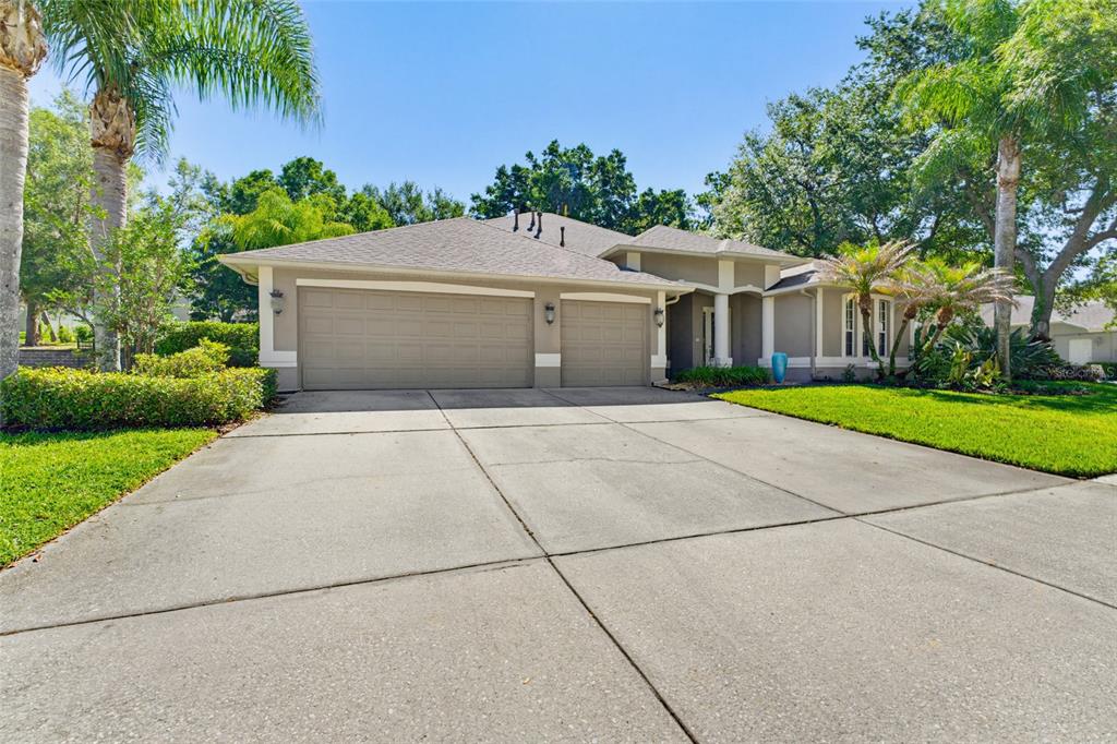 A single-story house with a three-car garage, concrete driveway, and palm trees in the yard — 62 CAMELOT RIDGE DRIVE, BRANDON, FL