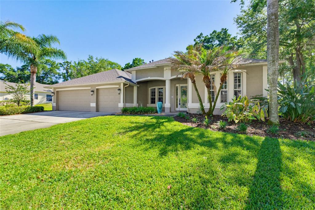 A single-story house with a two-car garage, beige stucco exterior, and a landscaped front yard — 62 CAMELOT RIDGE DRIVE, BRANDON, FL