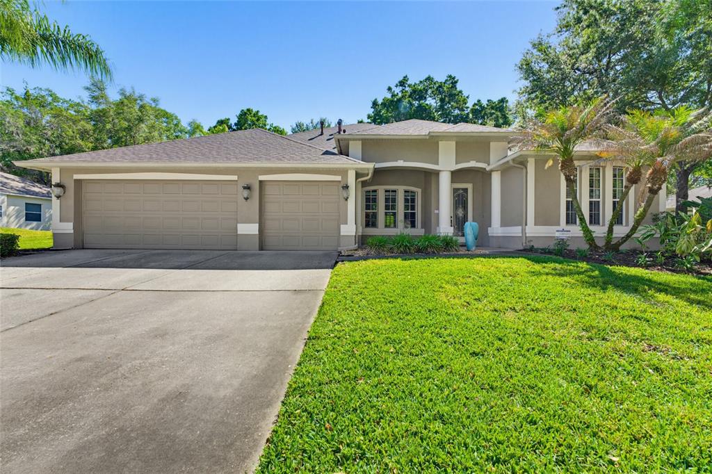 A single-story house with a two-car garage, beige stucco exterior, and a front lawn — 62 CAMELOT RIDGE DRIVE, BRANDON, FL