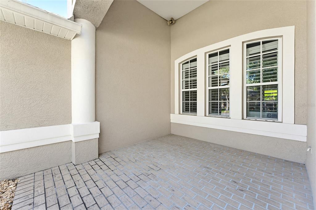 A covered patio features light-colored brick pavers, a white column, and three windows — 62 CAMELOT RIDGE DRIVE, BRANDON, FL