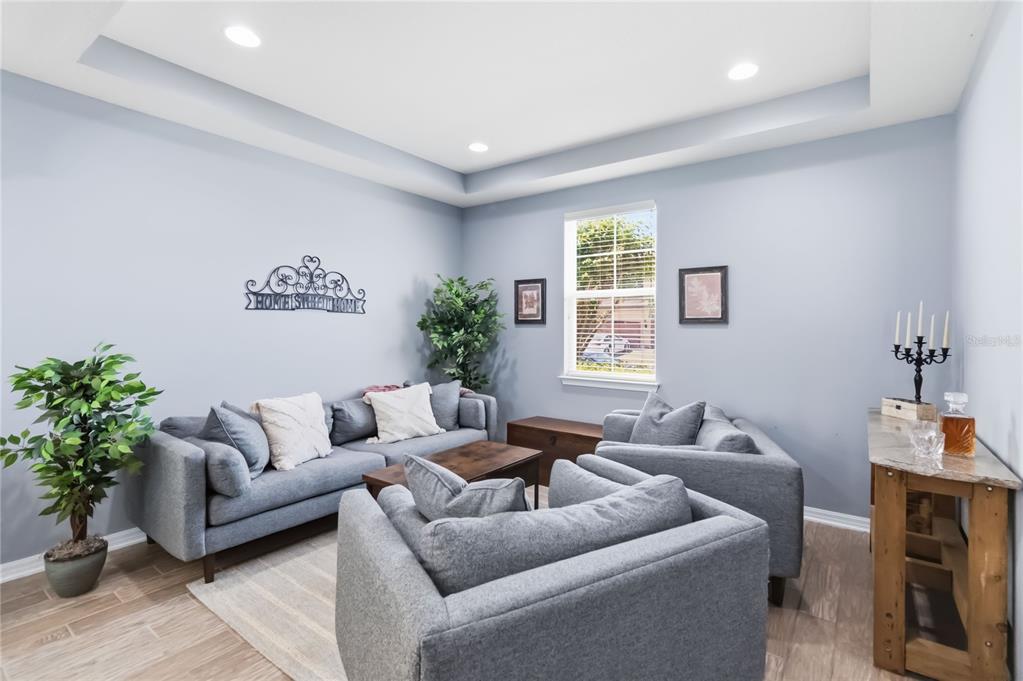 A living room features gray walls, a tray ceiling, gray furniture, and wood-look tile flooring — 5053 TORCHWOOD DRIVE, MINNEOLA, FL