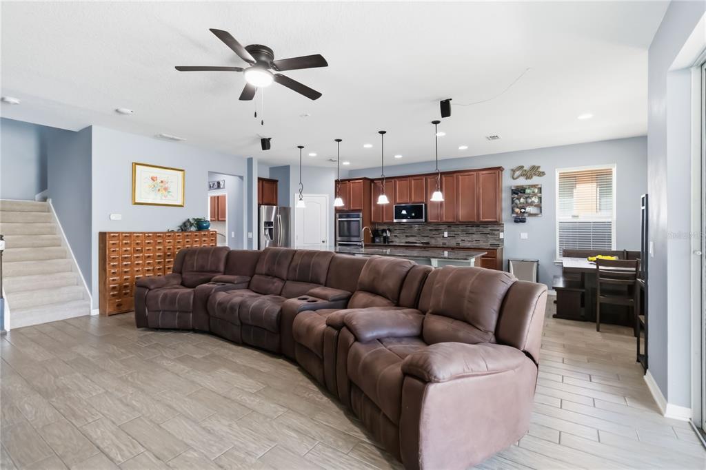 A large brown sectional sofa sits in an open-concept living room with a kitchen behind — 5053 TORCHWOOD DRIVE, MINNEOLA, FL