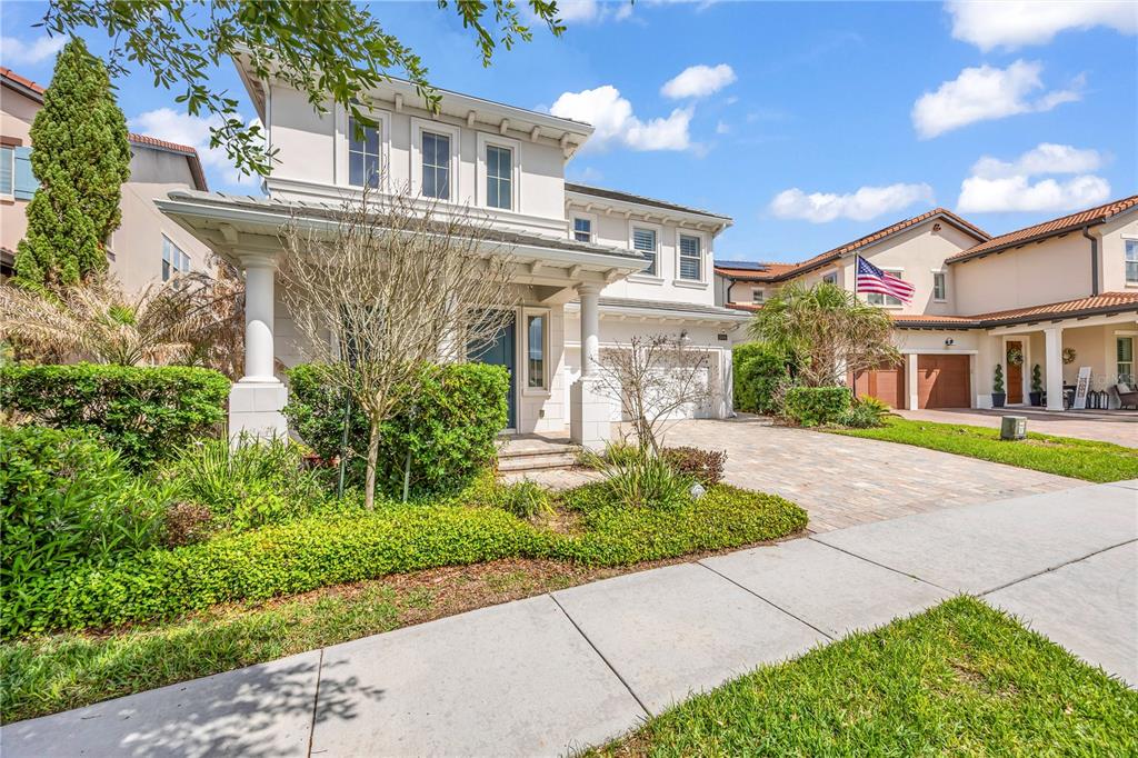 A two-story house with a paved driveway, front porch, and manicured landscaping under a blue sky — 15594 SHOREBIRD LANE, WINTER GARDEN, FL